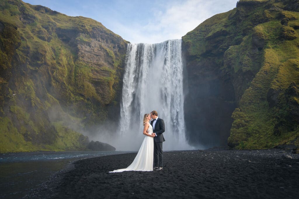 Couple in wedding attire standing in front of Skógafoss waterfall for their Iceland elopement