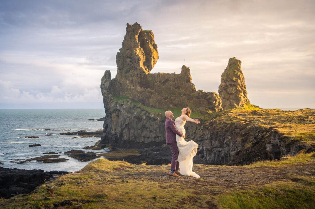 Groom lifting bride in front of a rock formation at golden hour on Snæfellsnes peninsula in Iceland