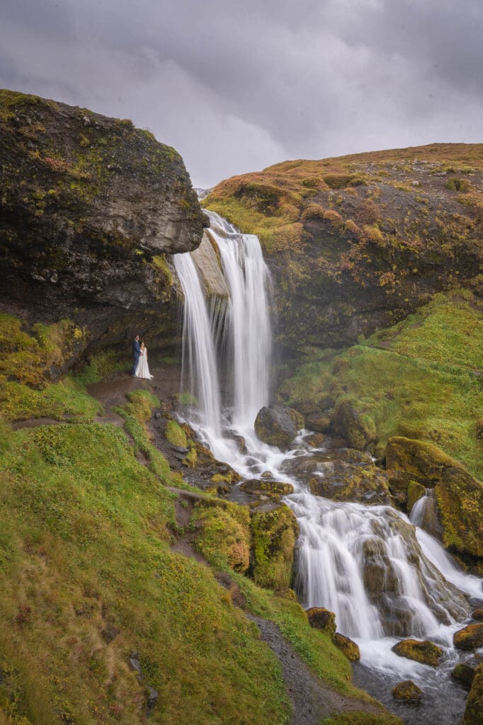 Bride and groom standing behind a waterfall in West Iceland