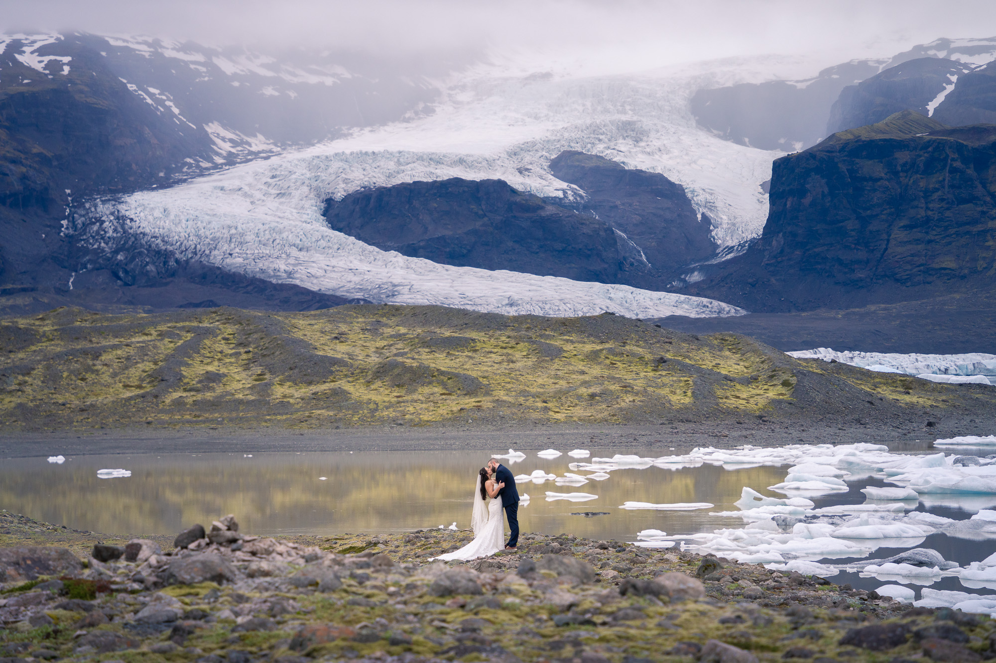 A wedding couple is kissing in front of stunning glacier and mountain background